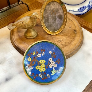 May include: A gold bird figurine with a round base, a gold oval picture frame with a decorative border, and a small blue and gold trinket dish with a floral design and a bird.