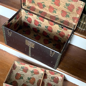 May include: An open, antique trunk with a dark brown exterior and a floral patterned interior. The trunk has metal hardware and a matching tray. The interior lining features a repeating pattern of red flowers and green leaves on a beige background.