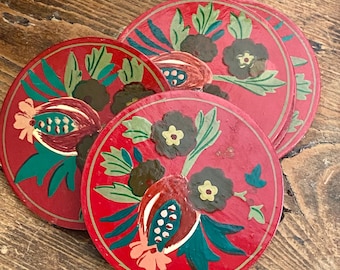 Puede incluir: Juego de cuatro posavasos rojos con diseños florales. Cada posavasos presenta un borde dorado y flores pintadas a mano en verde, marrón y dorado. Los posavasos están dispuestos sobre una superficie de madera.