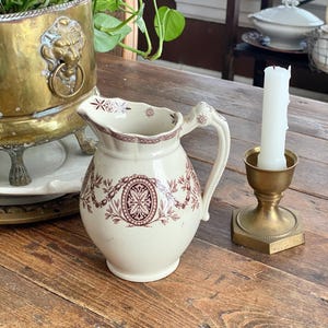 May include: A white ceramic mug with a black handle and the text "But First, Coffee" in a bold, black font. The mug is set against a blurred background, suggesting a cozy setting. The mug appears to be approximately 4 inches tall.