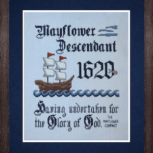May include: A white cross-stitch embroidery with blue and brown accents. The embroidery features a ship with sails, the text "Mayflower Descendant 1620", and the phrase "Daring undertaken for the Glory of God. The Mayflower Compact".