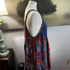 Puede incluir: Una blusa sin mangas con un vibrante estampado de cachemira en rojo, verde azulado y morado. La blusa presenta un canes&uacute; y tirantes de ganchillo azul marino. La prenda se exhibe en un maniqu&iacute;.