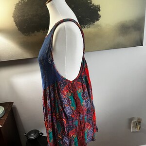 Puede incluir: Una blusa sin mangas con un panel de encaje azul marino y un estampado paisley vibrante en rojo, verde y morado. La blusa se muestra en un maniqu&iacute;, mostrando su dise&ntilde;o fluido y detalles intrincados. Las correas tambi&eacute;n tienen un estampado.