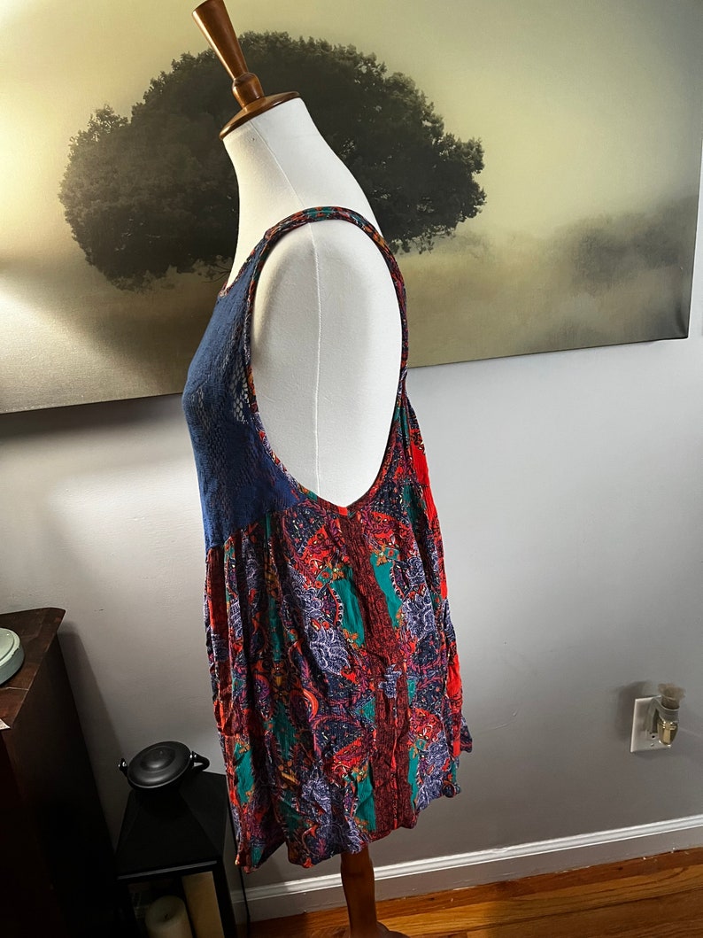 Puede incluir: Una blusa sin mangas con un panel de encaje azul marino y un estampado paisley vibrante en rojo, verde y morado. La blusa se muestra en un maniqu&iacute;, mostrando su dise&ntilde;o fluido y detalles intrincados. Las correas tambi&eacute;n tienen un estampado.