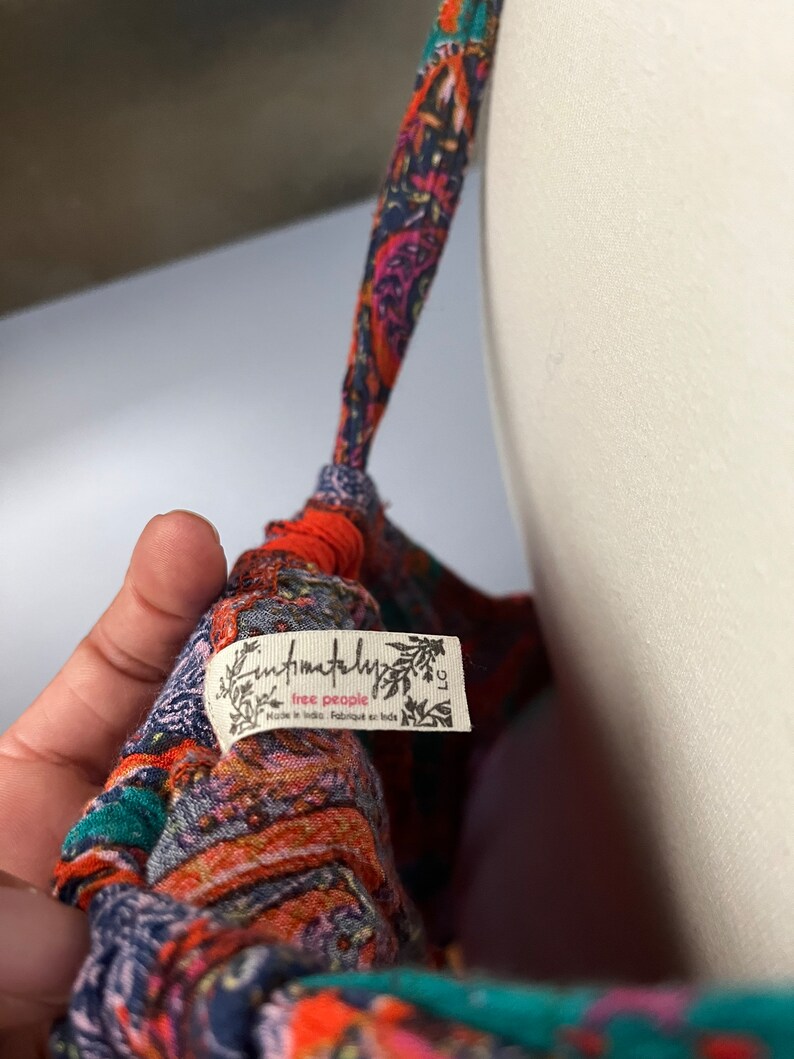Puede incluir: Primer plano de una prenda estampada colorida con una etiqueta que dice "Intimately Free People". La tela presenta una mezcla de tonos naranja, azul y verde azulado. La prenda est&aacute; sobre un maniqu&iacute;.