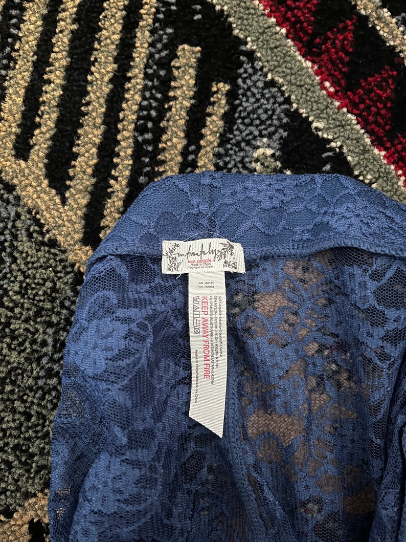 Pode incluir: Um top de renda azul com uma etiqueta branca que diz "Free People" e "Keep Away From Fire".