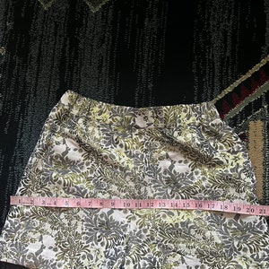 May include: White shorts with a green and yellow floral pattern. The shorts are measured with a tape measure, showing a length of 21 inches.