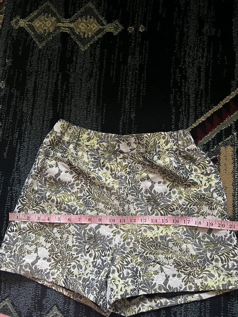 May include: White shorts with a green and yellow floral pattern. The shorts are measured with a tape measure, showing a length of 21 inches.