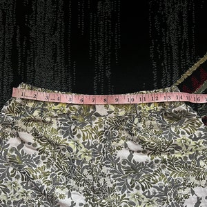 May include: A white fabric skirt with a green and gold floral pattern. The skirt has a waistband with a pink measuring tape that reads "1 2 3 4 5 6 7 8 9 10 11 12 13 14 15 16".