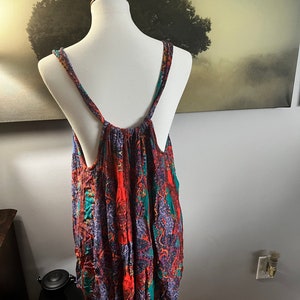 Puede incluir: Una blusa sin mangas con un vibrante estampado de cachemira en tonos rojos, verde azulado y morado. La blusa se exhibe en un maniqu&iacute;, mostrando su dise&ntilde;o fluido y su ajuste c&oacute;modo. Las correas son finas y la tela parece ligera.