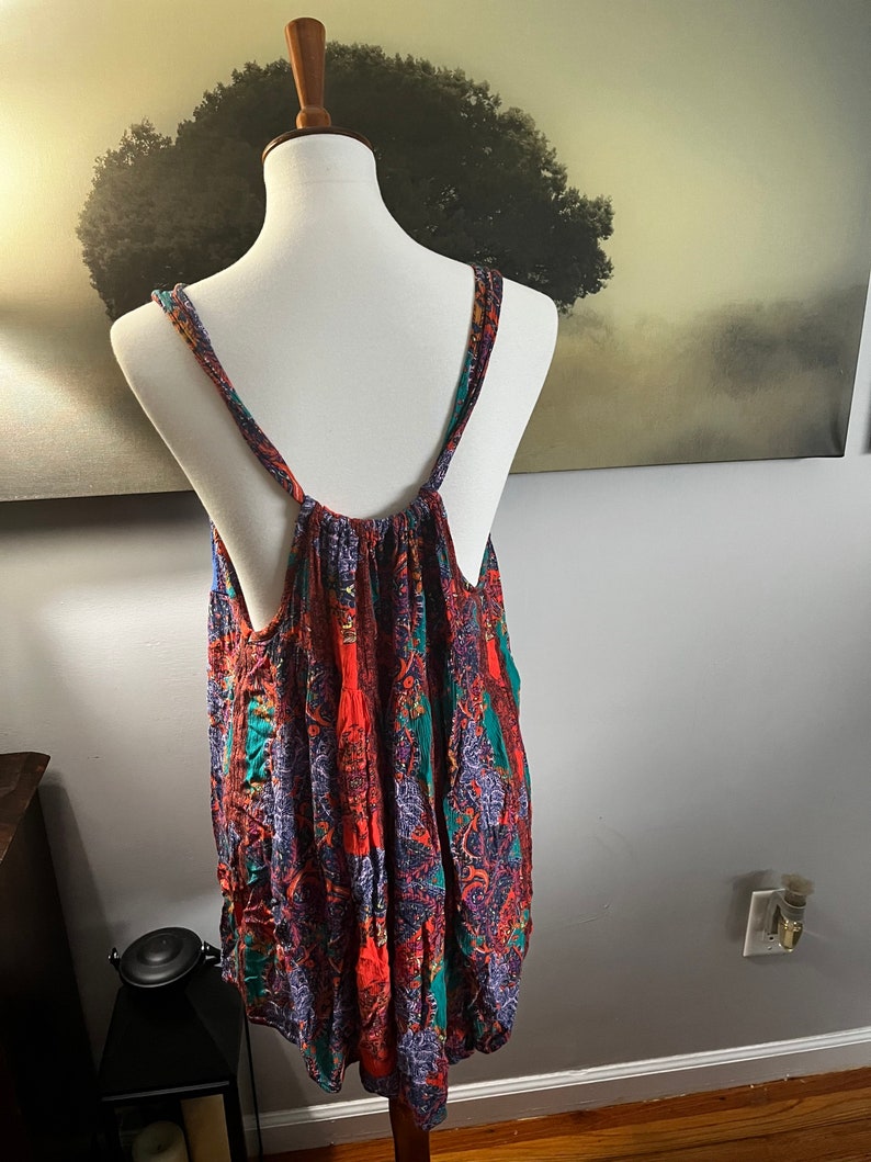Puede incluir: Una blusa sin mangas con un vibrante estampado de cachemira en tonos rojos, verde azulado y morado. La blusa se exhibe en un maniqu&iacute;, mostrando su dise&ntilde;o fluido y su ajuste c&oacute;modo. Las correas son finas y la tela parece ligera.