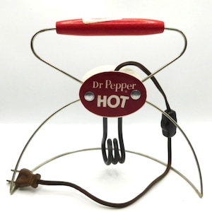 May include: A vintage electric beverage heater featuring a red wooden handle and a metal wire frame. A central oval red plaque displays the white text Dr Pepper and HOT. A brown electrical cord with a plug and a small black switch is attached.