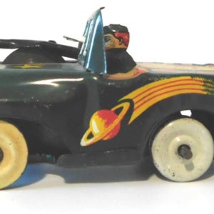 May include: Vintage toy car in dark green with yellow and red accents. The car features a driver figure, yellow wheels, and a graphic of a planet with a yellow and red comet trail. A classic collectible.