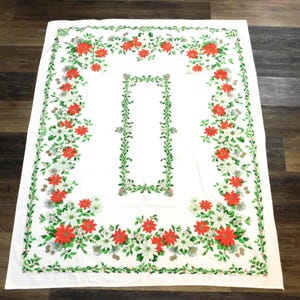 May include: White rectangular tablecloth with a floral design. The tablecloth features a border of red poinsettias, white flowers, and green leaves. A central rectangular design mirrors the border's floral elements.