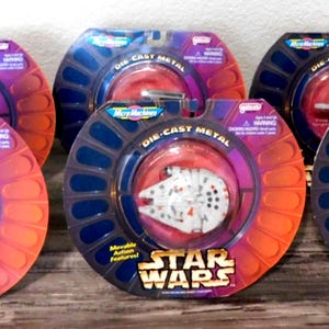 May include: Six Star Wars Micro Machines die-cast metal vehicles in their original packaging. Each package is a circular shape with a blue and orange color scheme. The Star Wars logo is visible on the packaging.