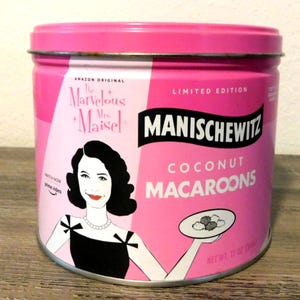 May include: A pink, limited edition Manischewitz coconut macaroon tin featuring a retro illustration of a woman holding a plate of macaroons. The tin has the text "The Marvelous Mrs. Maisel" and "Amazon Original".
