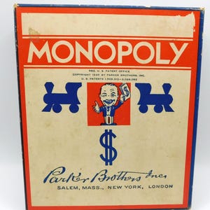 May include: Vintage Monopoly board game box with a red and blue design. The box features the word "MONOPOLY" in large letters, a cartoon character, train graphics, and the Parker Brothers logo. The box is from 1935.