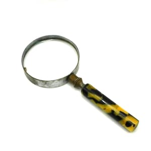 May include: A magnifying glass featuring a circular lens held by a silver-toned metal frame. The handle is cylindrical with a mottled black and yellow tortoiseshell pattern, connected to the frame by a small, decorative brass-colored metal ferrule.