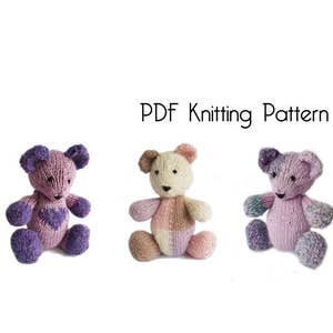 Può includere: Tre orsacchiotti di peluche a maglia in diverse combinazioni di colori rosa, viola e crema. Gli orsacchiotti sono seduti su uno sfondo bianco. Modello di maglia PDF.