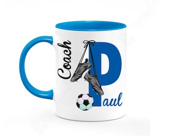 Op de afbeelding: Witte keramische mok met een blauwe rand en handvat. De mok heeft een blauwe letter "P" met een voetbal en twee zwarte voetbalschoenen die eraan hangen. De tekst "Coach Paul" staat op de mok.