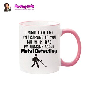 May include: White ceramic mug with a pink rim and handle. The mug features a black and white illustration of a person with a metal detector and the text "I might look like I'm listening to you but in my head I'm thinking about Metal Detecting."