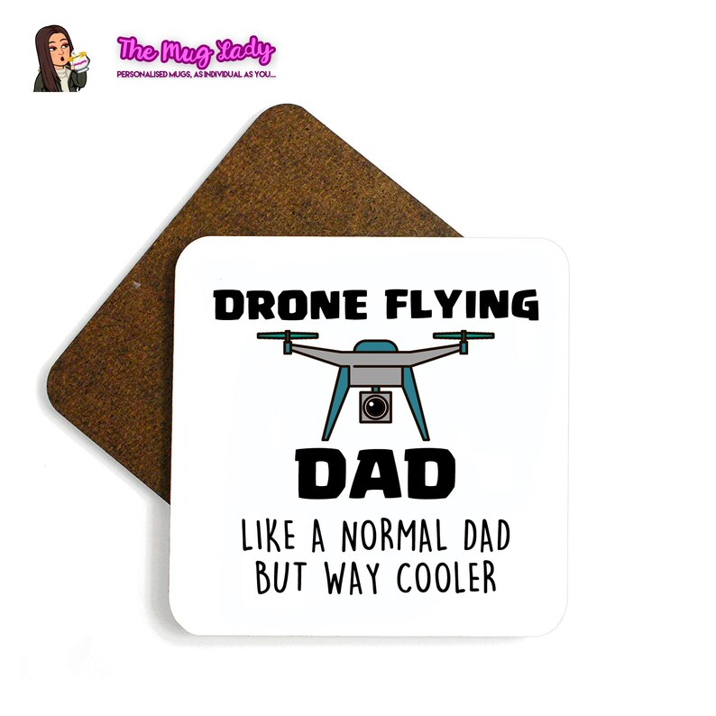 Op de afbeelding: Een witte vierkante onderzetter met de tekst "DRONE FLYING DAD LIKE A NORMAL DAD BUT WAY COOLER" en een drone-afbeelding. Een bruine vierkante onderzetter staat erachter. Het logo van The Mug Lady staat linksboven.