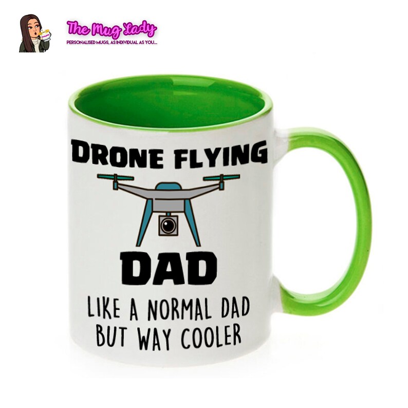 Op de afbeelding: Witte keramische mok met een groene binnenkant en handvat. De mok heeft de tekst "DRONE FLYING DAD" met een drone-afbeelding en de zin "LIKE A NORMAL DAD BUT WAY COOLER". Het logo van The Mug Lady staat linksboven.