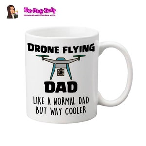 Op de afbeelding: Witte keramische mok met de tekst "DRONE FLYING DAD LIKE A NORMAL DAD BUT WAY COOLER" en een drone-afbeelding in zwart, blauwgroen en grijs. Het logo van The Mug Lady staat linksboven.