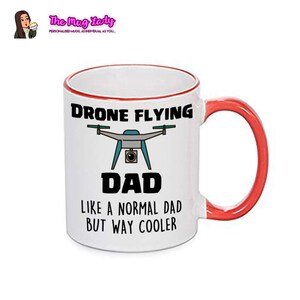 Op de afbeelding: Witte keramische mok met een rode handgreep en rand. De mok heeft de tekst "DRONE FLYING DAD LIKE A NORMAL DAD BUT WAY COOLER" met een drone-afbeelding. Het logo van The Mug Lady staat linksboven.