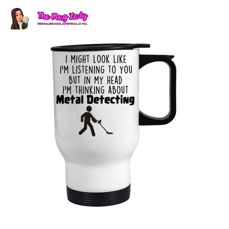 May include: White travel mug with a black handle and lid. The mug has a black and white illustration of a person with a metal detector and the text "I might look like I'm listening to you but in my head I'm thinking about Metal Detecting."