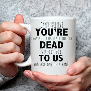 May include: White ceramic coffee mug with black text that reads "Can't believe you're leaving. This place will be dead without you. To us. You are one of a kind."