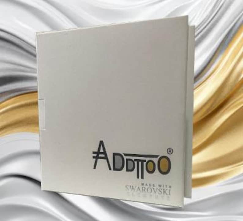 Puede incluir: Caja de cart&oacute;n blanca con el logotipo "Addtoo" impreso en negro y el texto "Made with Swarovski Elements" impreso en gris.