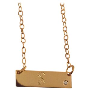 May include: Gold chain necklace with a gold bar pendant. The bar has a small diamond and the letter 'S' engraved on it.