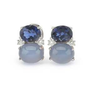 May include: A pair of silver earrings with blue and gray gemstones. The earrings feature a larger, round, gray gemstone with a smaller, round, blue gemstone on top. The earrings are set in silver and have a simple, elegant design.