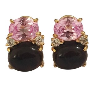 May include: A pair of gold earrings with black and pink gemstones. The earrings feature a round black gemstone surrounded by smaller diamonds and topped with a round pink gemstone.