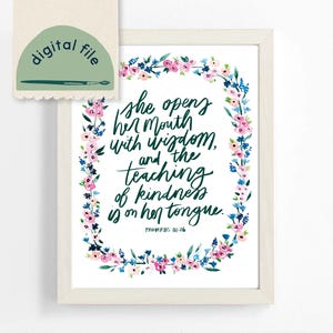 May include: A framed print with a white border features a floral wreath in pink and blue watercolor. The text reads "she opens her mouth with wisdom, and the teaching of kindness is on her tongue. Proverbs 31:26." A digital file icon is in the upper left.