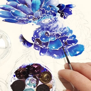Puede incluir: Un primer plano de una pintura de acuarela de un p&aacute;jaro azul con una cresta azul y morada. El artista est&aacute; usando un pincel peque&ntilde;o para agregar detalles a la pintura. Una paleta de acuarela con varios tonos de azul, morado y negro es visible en primer plano.