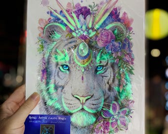 Può includere: Una stampa artistica rettangolare raffigurante il ritratto di una tigre bianca adornata con fiori viola e rosa, accenti verde brillante e un copricapo centrale con gemma. È allegato un piccolo cartoncino blu con il testo Spirit Animal Totem Series.