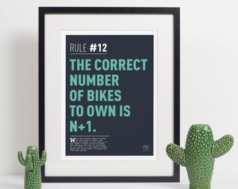 May include: A black framed poster with a white background and blue text that reads "RULE #12 THE CORRECT NUMBER OF BIKES TO OWN IS N+1."