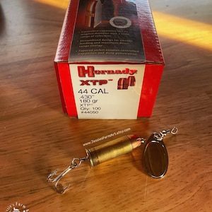 May include: A handmade fishing lure made from a .430" 180 grain Hornady XTP bullet. The lure is gold with a silver blade and is attached to a box of Hornady XTP bullets. The box is red and white and has the text "Hornady XTP" and "44 CAL" on it. The box also has the text ".430" 180 gr XTP" and "Qty: 100 #44050".