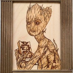 May include: A wood-burned image of a character from the movie Guardians of the Galaxy, Groot, holding a small device with the text "I am Groot" on it.