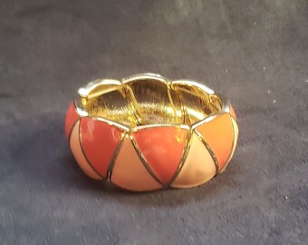 May include: A gold-toned bracelet with a geometric design. The bracelet is made of metal and has a pink and peach enamel finish.