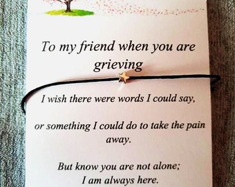 May include: A white card with a black string bracelet and a small gold star charm. The card has a drawing of a pink cherry blossom tree and the text "To my friend when you are grieving. I wish there were words I could say, or something I could do to take the pain away. But know you are not alone; I am always here. Wear this to remember I am always near."