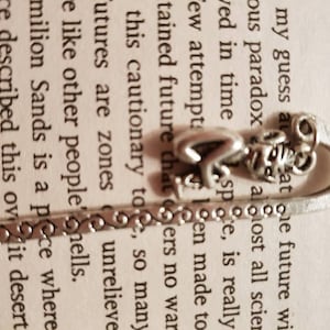 May include: Silver bookmark with a heart, a butterfly, and a decorative design. The bookmark is resting on a page of a book with the word "Preface" printed at the top of the page.