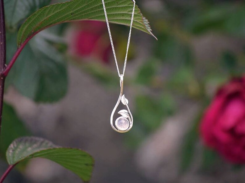 May include: A silver necklace with a delicate pendant featuring a round, light pink gemstone surrounded by silver leaves.