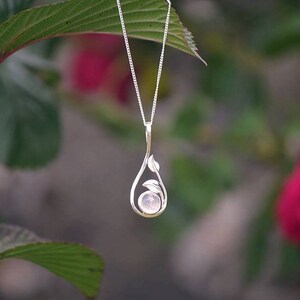 May include: A silver necklace with a delicate pendant featuring a round, light pink gemstone surrounded by silver leaves.