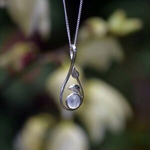 May include: A silver necklace with a delicate pendant featuring a moonstone set in a leaf design.