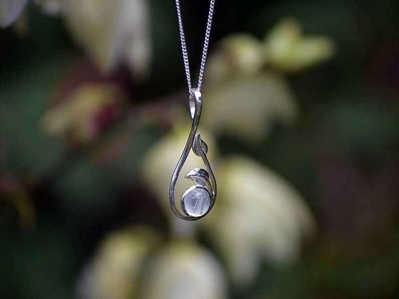 May include: A silver necklace with a delicate pendant featuring a moonstone set in a leaf design.