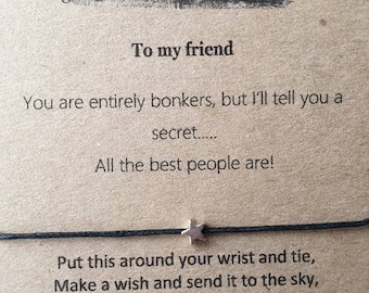 May include: A brown card with a black and white illustration of Alice in Wonderland characters having tea. The card has the text "To my friend" and "You are entirely bonkers, but I'll tell you a secret..... All the best people are!"  The card also has a black string with a silver star charm attached.