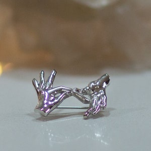 May include: Silver brooch depicting two hands clasped together, representing love and unity.